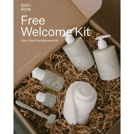 An Act and Acre image ad: an open cardboard box of shampoo, conditioner, serums, a scalp brush and a towel on shredded paper