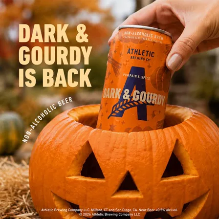 An Athletic Brewing image ad: a hand lifting a Dark and Gourdy can out of a carved pumpkin under the line it is back