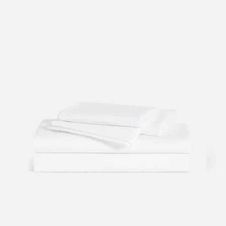 A Brooklinen image ad: a neatly folded stack of white sheets and pillowcases on a pale grey background