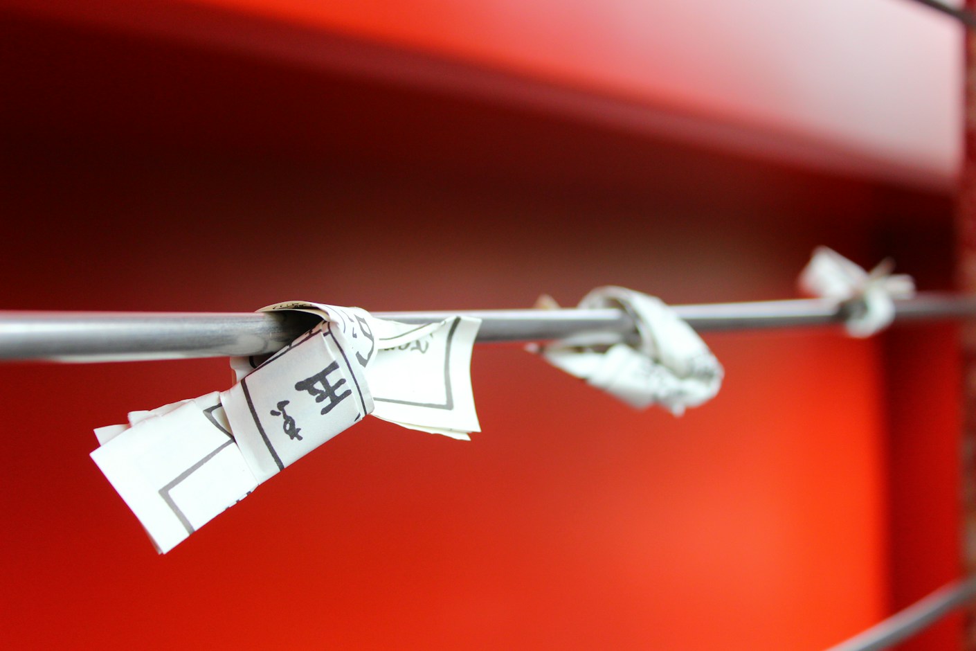 Paper price tags knotted onto a metal rail against a red wall